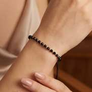Close-up of a wrist wearing a black beaded bracelet against a neutral background