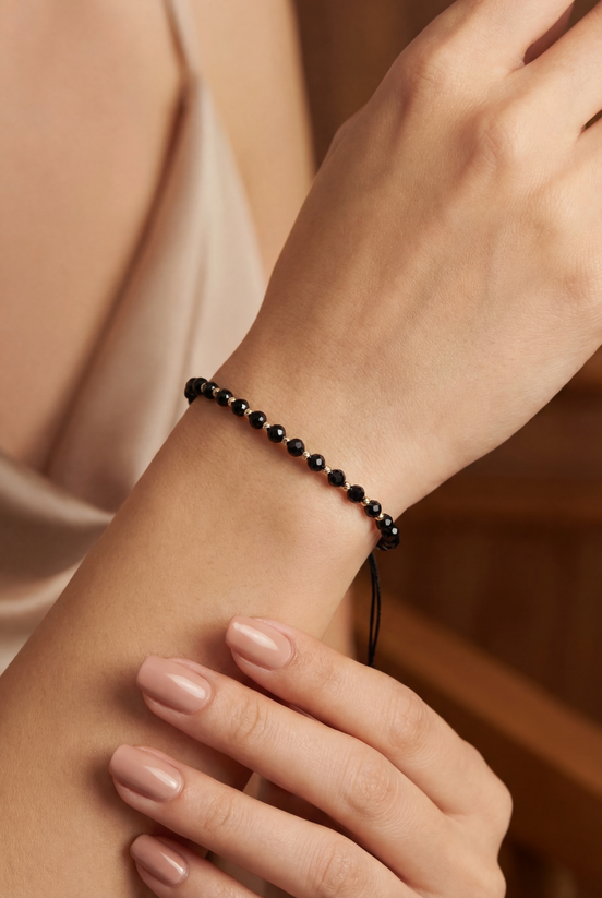 Close-up of a wrist wearing a black beaded bracelet against a neutral background