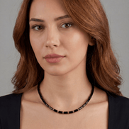 Woman wearing a black beaded necklace against a gray background