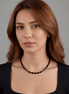 Woman wearing a black beaded necklace against a gray background