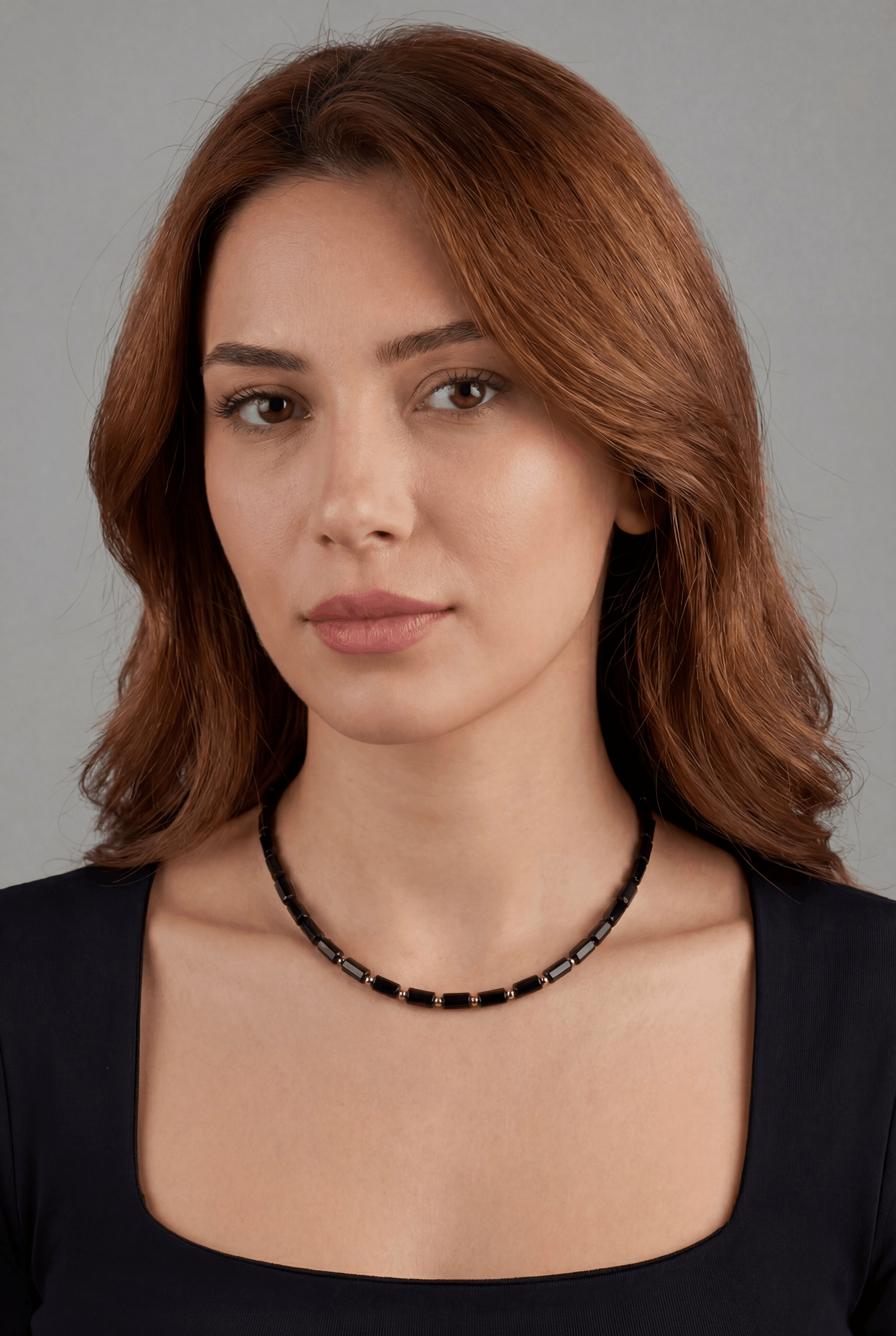Woman wearing a black beaded necklace against a gray background